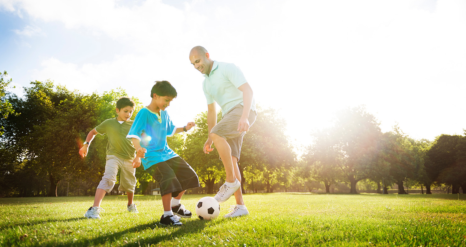 father playing soccer with his sons outside