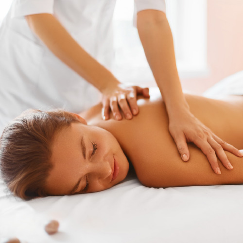 woman lays chest down on a massage table as a masseuse massages her upper back and shoulder