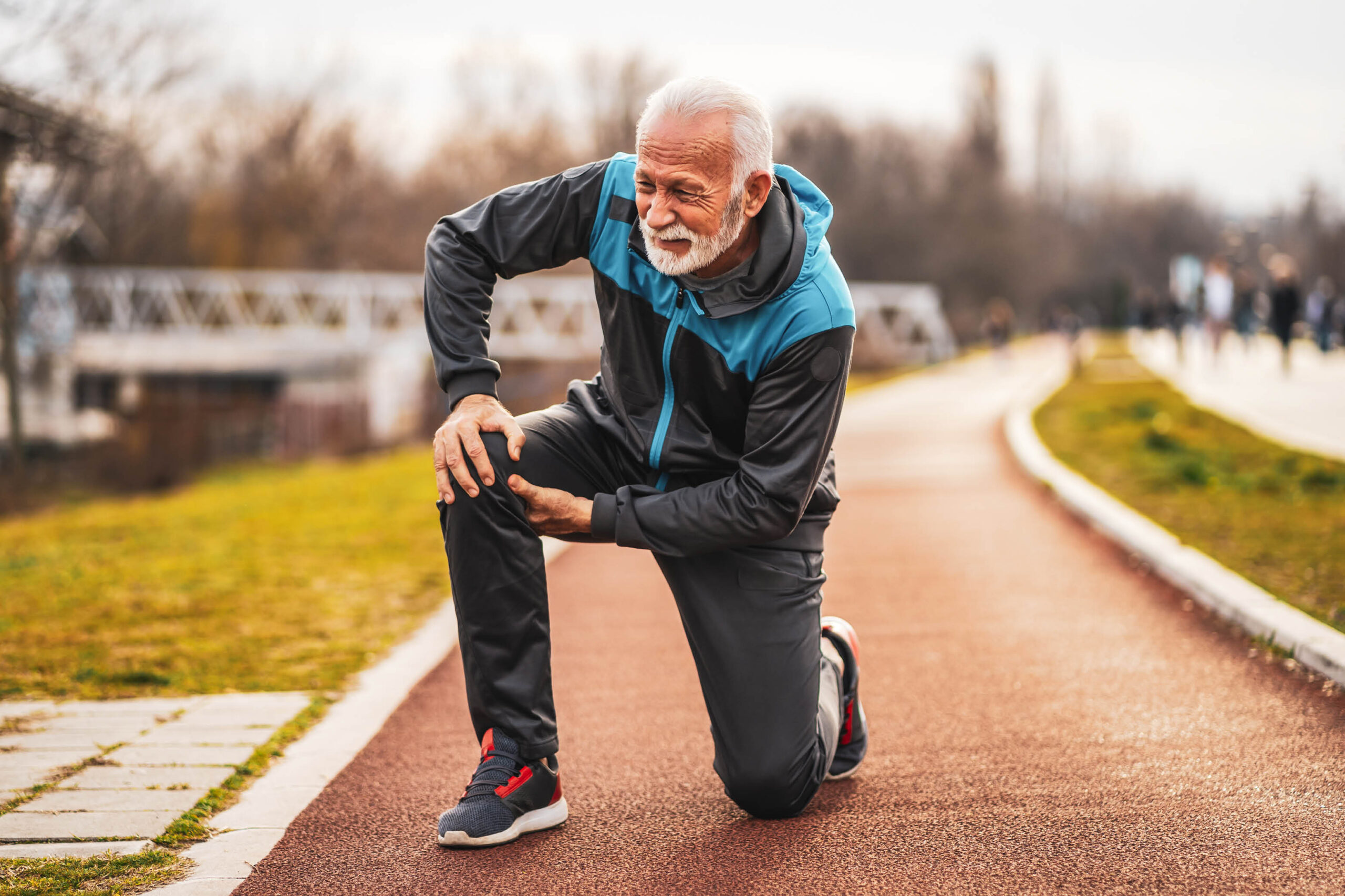 Man on a walk kneeling to hold painful knee