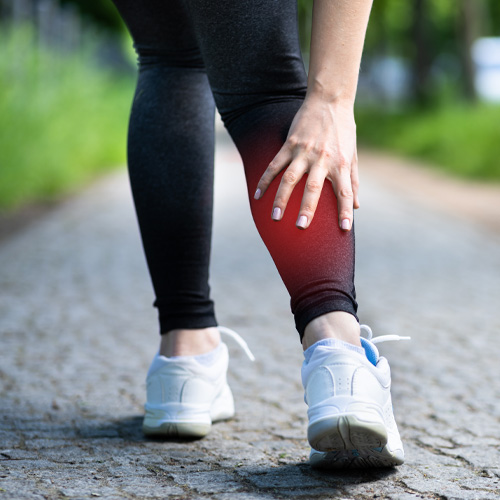 Woman on walk pausing to massage sore right calf