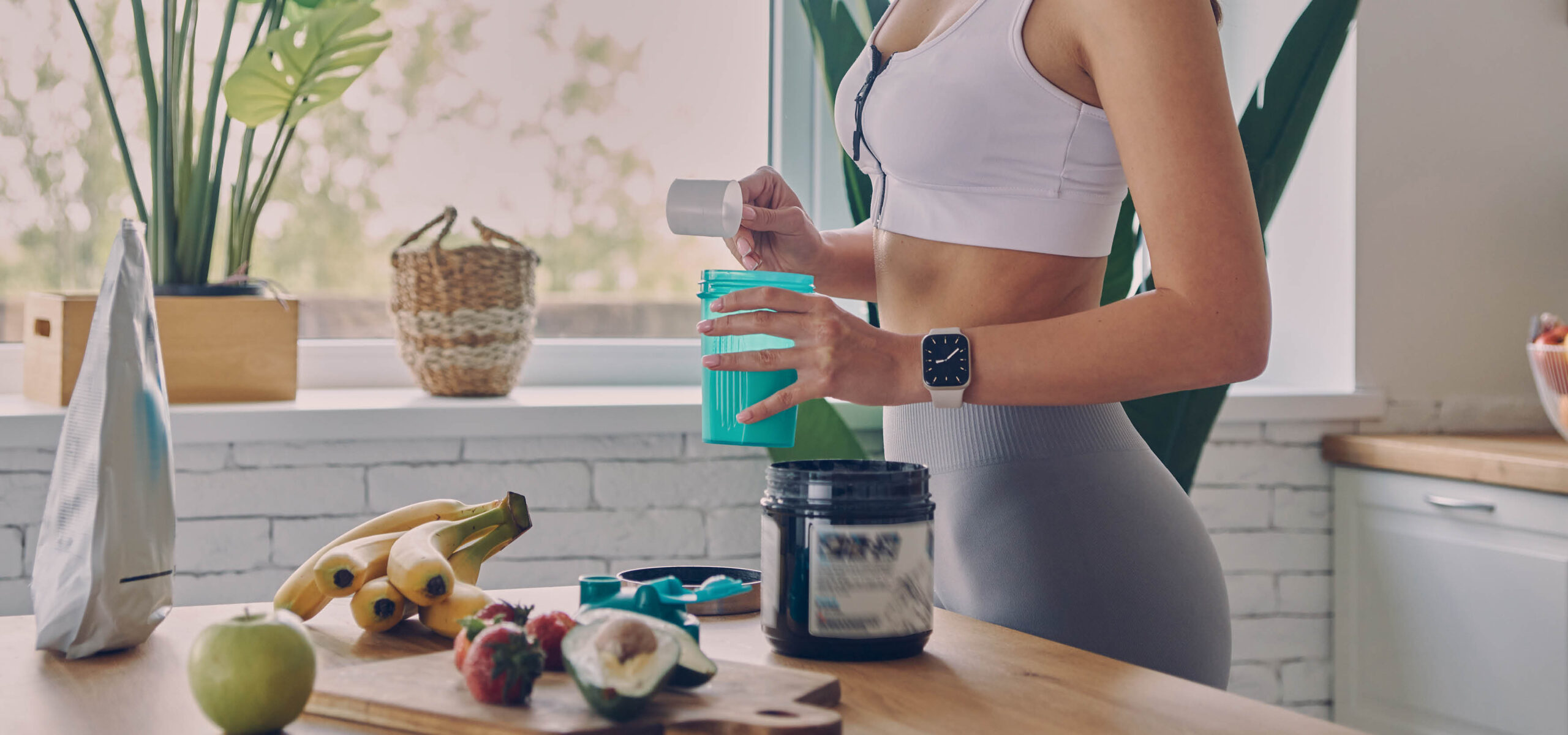Woman scooping protein powder into a healthy smoothie in her kitchen