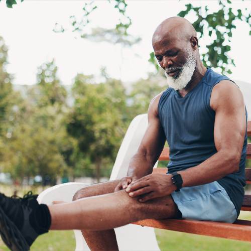 Athlete pausing workout to sit and massage knee on a park bench