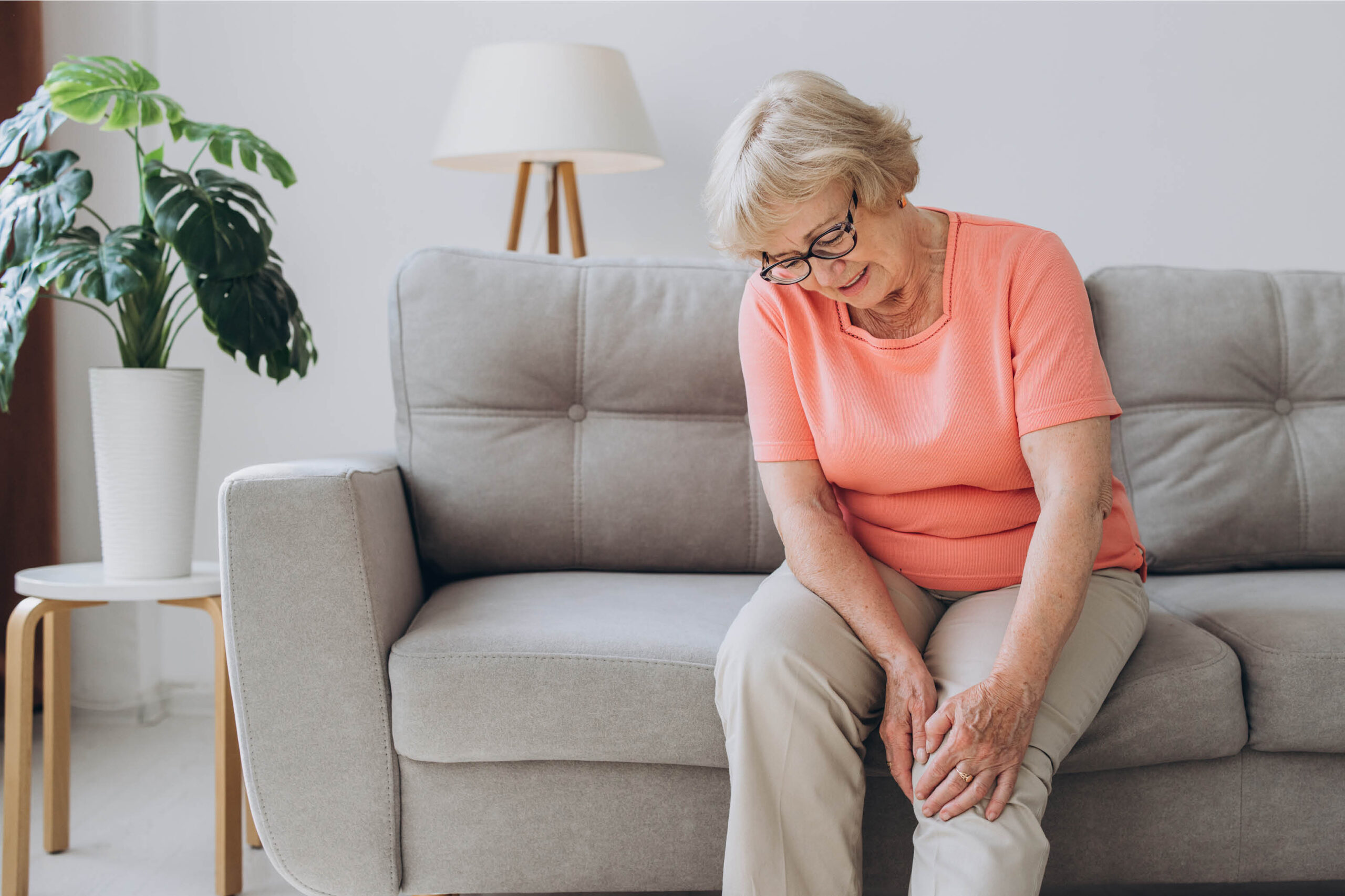Woman massaging her hurting left knee on the couch