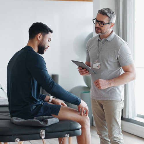 Patient describing knee pain to physical therapist on examination table